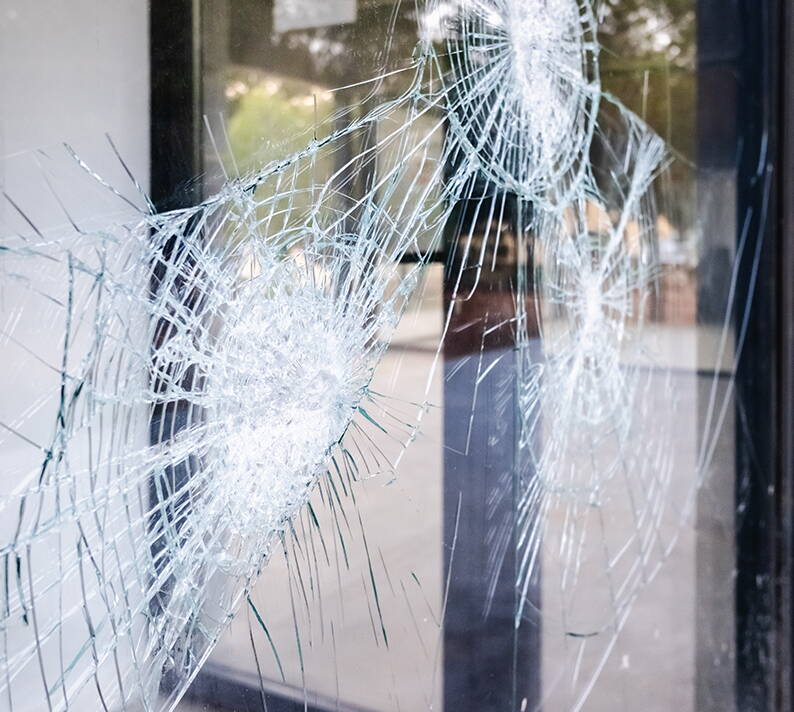 Gesprungene Fensterscheibe mit Einschlagspuren Nahaufnahme einer beschädigten Glasscheibe mit mehreren sternförmigen Rissen und Einschlagpunkten. Die Bruchstellen zeigen die typische Struktur von Sicherheitsglas nach einem starken Aufprall.